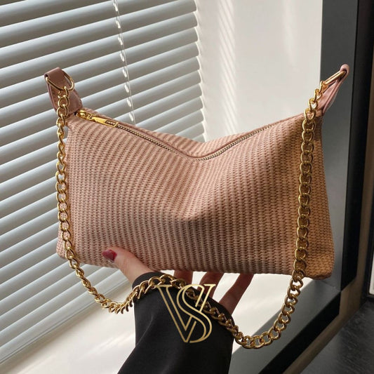 Light pink woven straw baguette bag featuring a gold chain strap and top zipper.