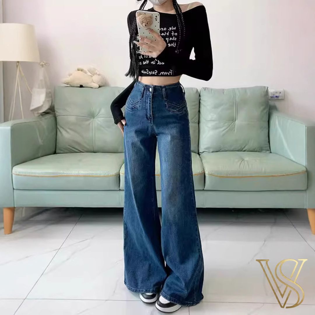 High-waisted medium blue wide-leg jeans with decorative front pocket stitching and a relaxed silhouette, styled with a black long-sleeve crop top for the vstyles collection.