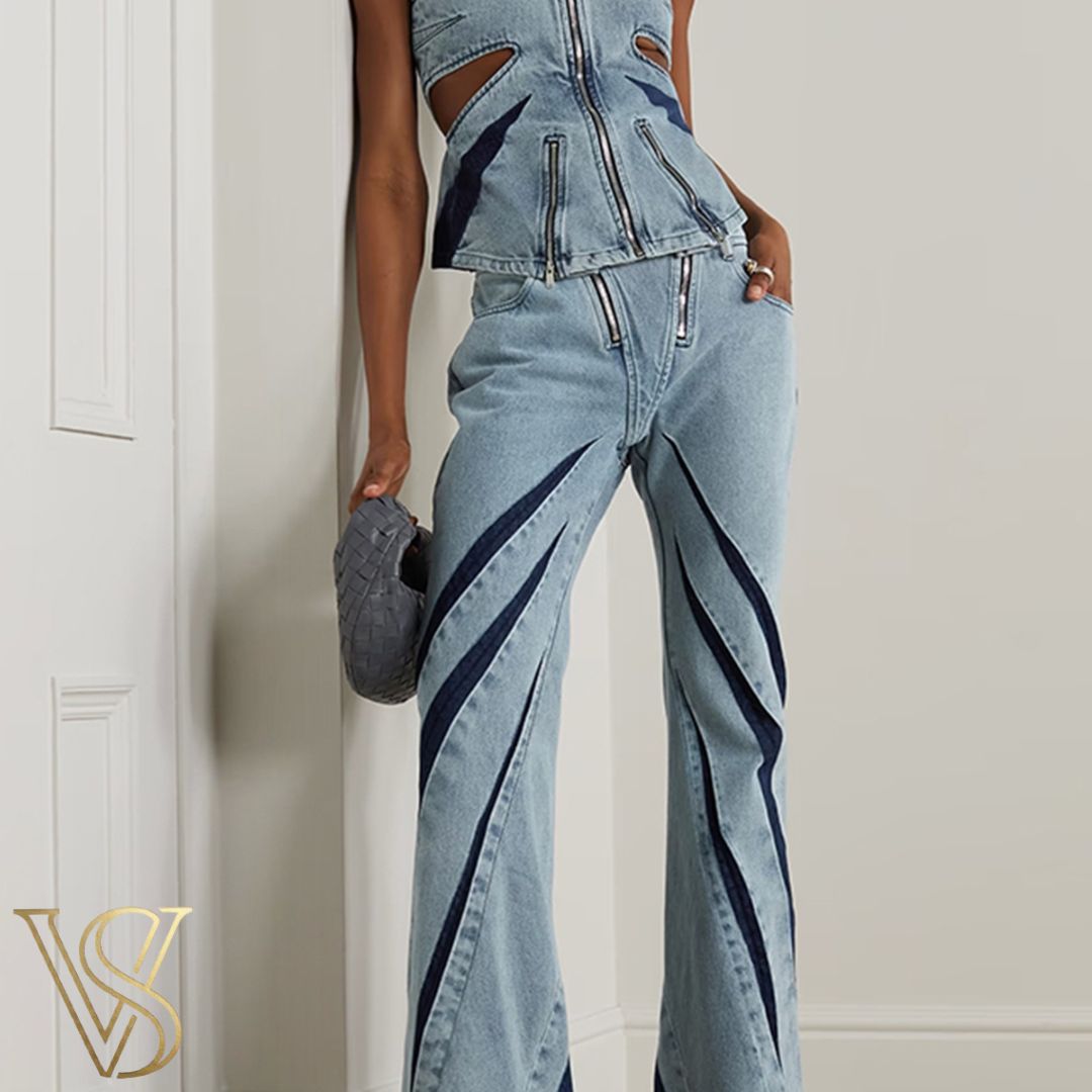 Avant-garde light blue denim two-piece featuring a strapless cutout top with multiple zippers and matching flared jeans with dark blue contrast paneling.