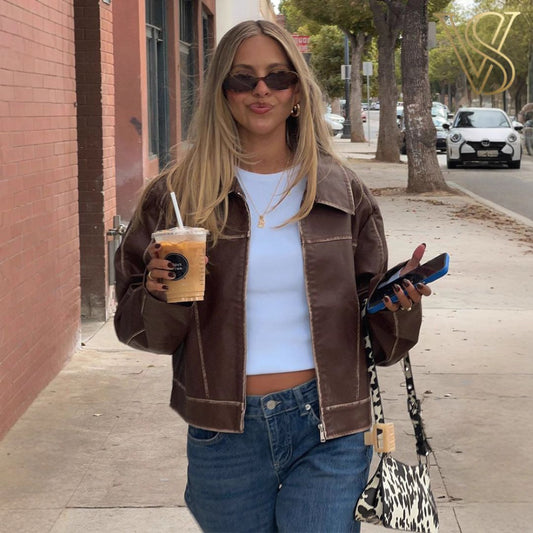 Distressed brown faux-leather zip-up jacket featuring a pointed collar, styled with a white crop top and blue jeans for a classic vstyles urban look.