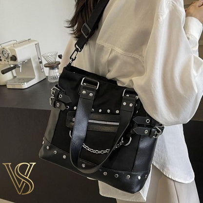 Edgy black punk-style tote bag featuring silver studs, side buckle straps, a slanted front zipper, and a decorative silver chain.