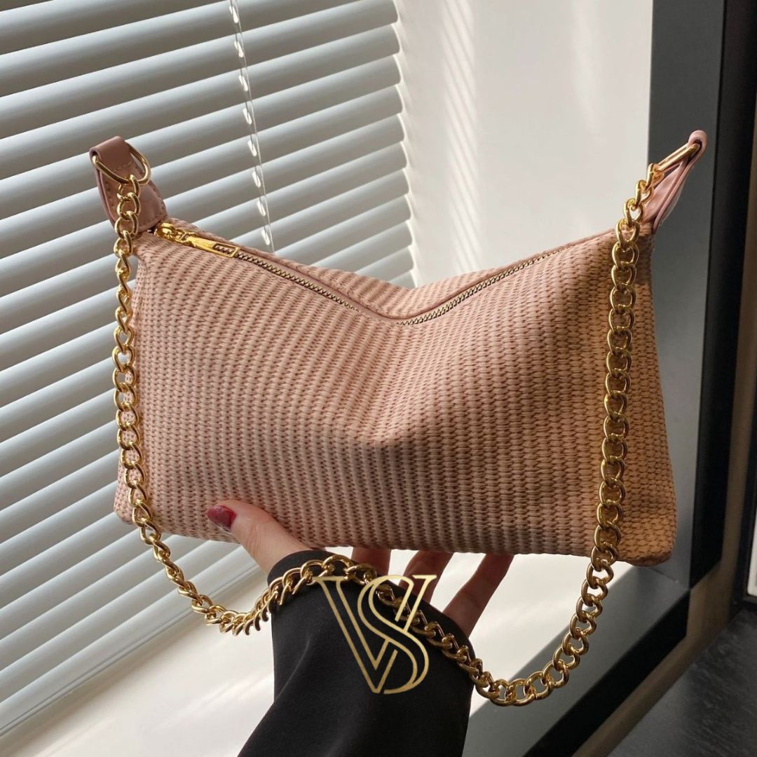 Light pink woven straw baguette bag featuring a gold chain strap and top zipper.