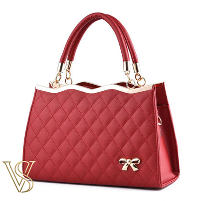 Sophisticated dark red quilted handbag with a scalloped gold top edge, dual handles, and a gold bow detail.