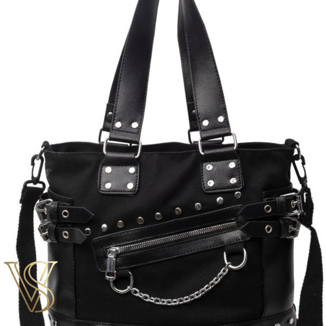 Edgy black punk-style tote bag featuring silver studs, side buckle straps, a slanted front zipper, and a decorative silver chain.