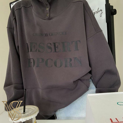 Oversized dark charcoal hoodie with tonal "CRUNCHY CRUNCHY DESSERT POPCORN" graphic text and a button-up collar detail, part of the vstyles ready-to-wear line.