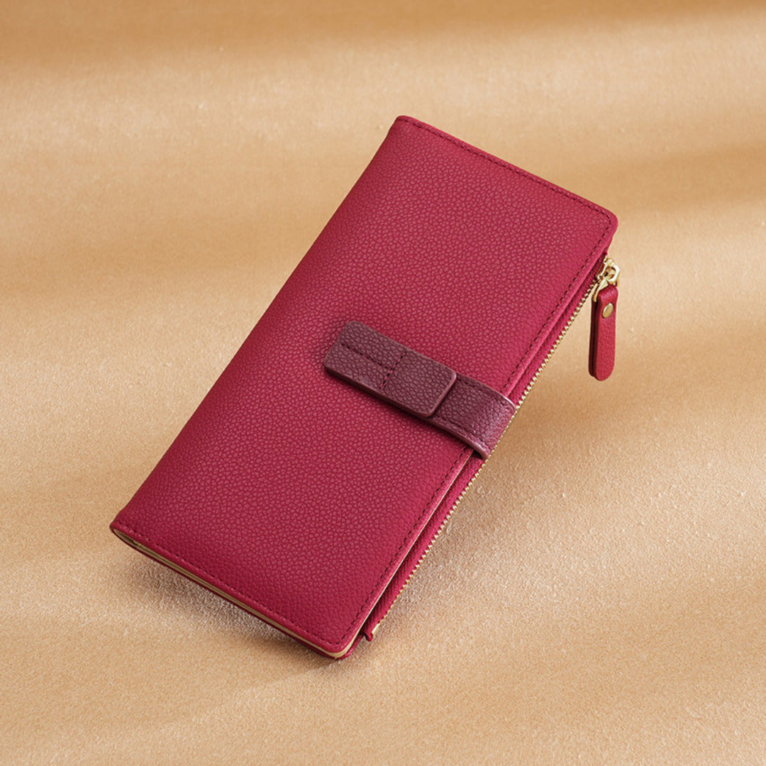 Deep magenta pebble-grain leather wallet with a tonal dark red strap and gold-tone zipper.