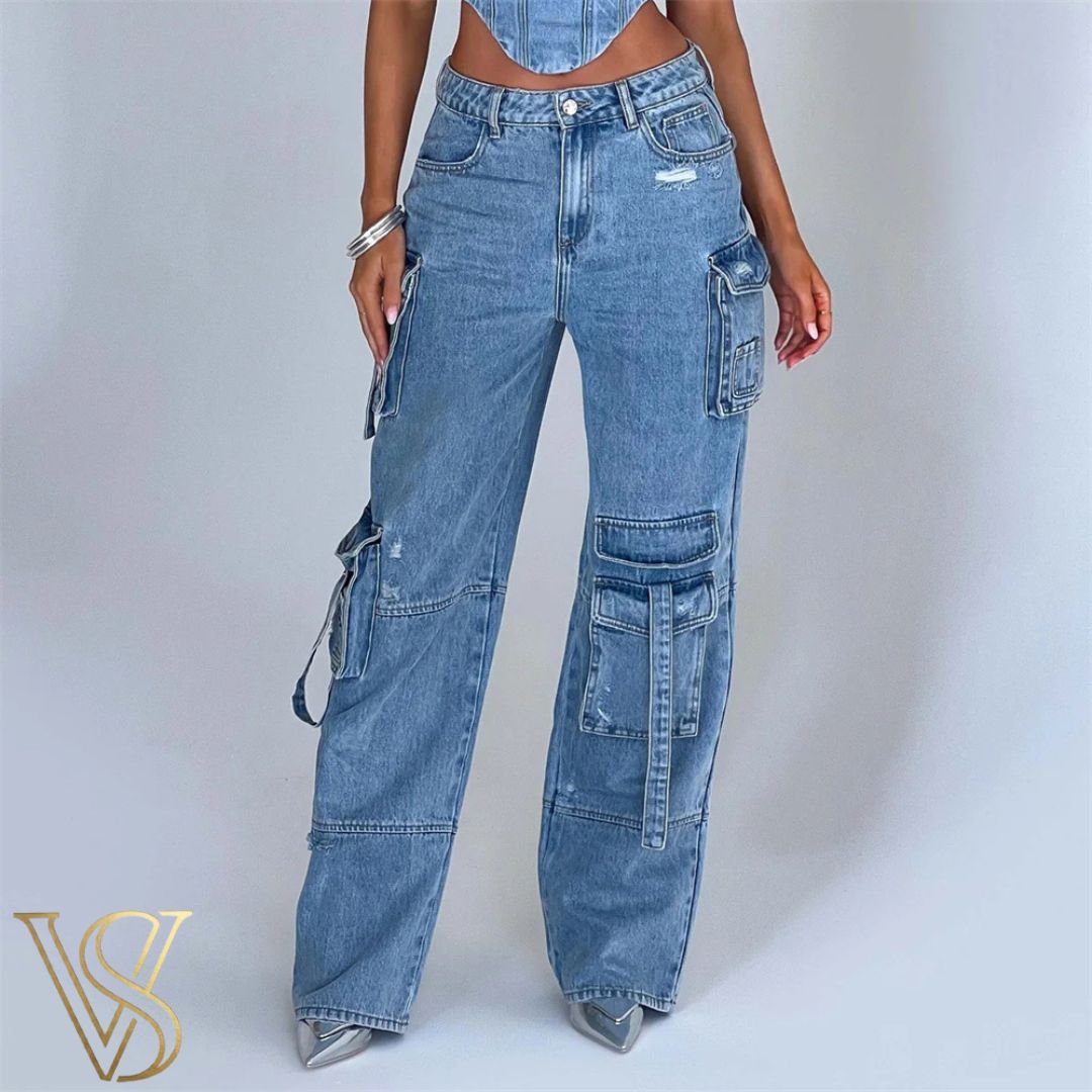 High-waisted medium wash denim cargo jeans featuring multiple utility pockets with decorative strap accents and a relaxed wide-leg fit for the vstyles collection.