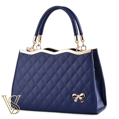 Classic navy blue quilted handbag featuring a gold-trimmed wavy top, matching handles, and a small gold bow.