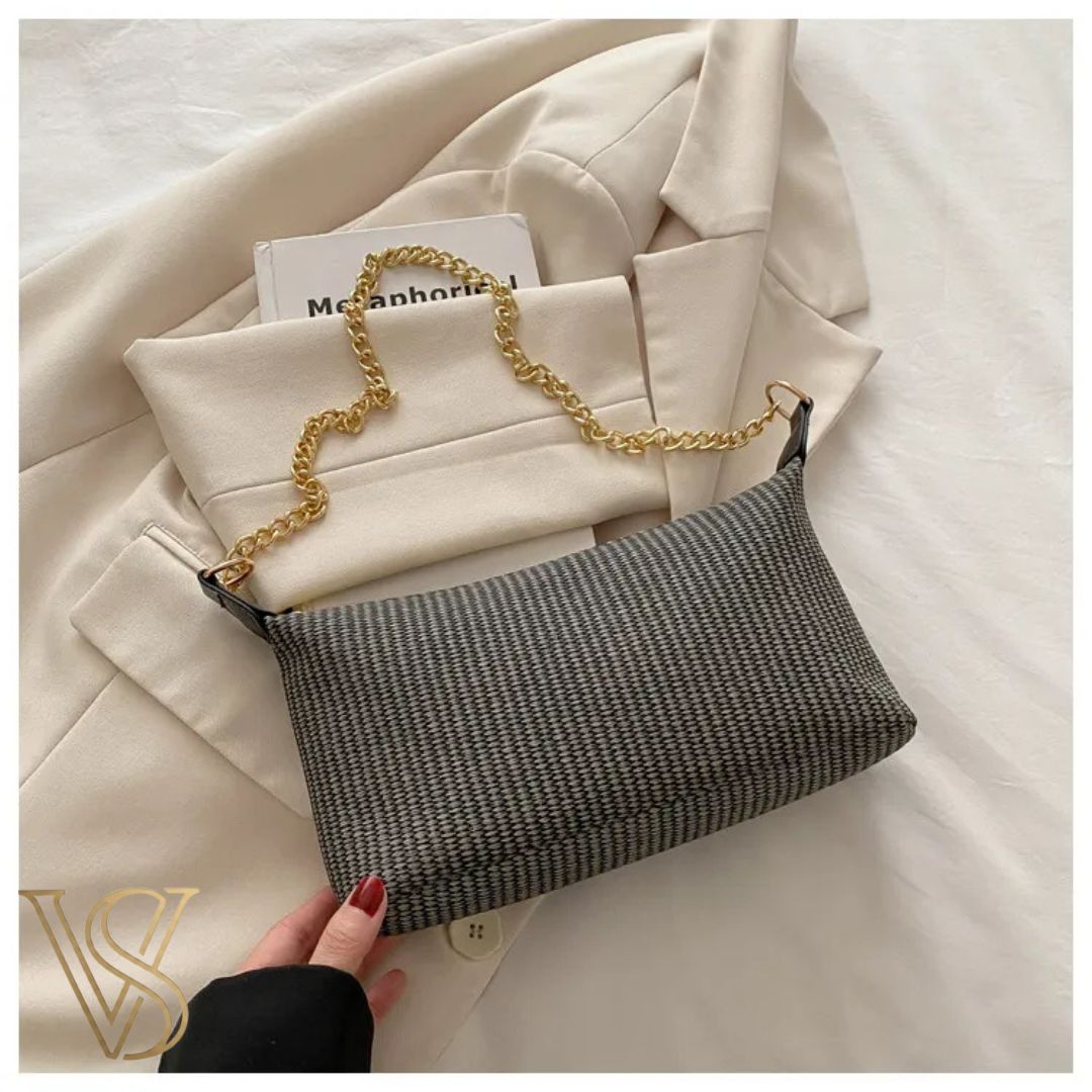 Black and grey patterned woven shoulder bag with a gold chain strap shown on a beige blazer.