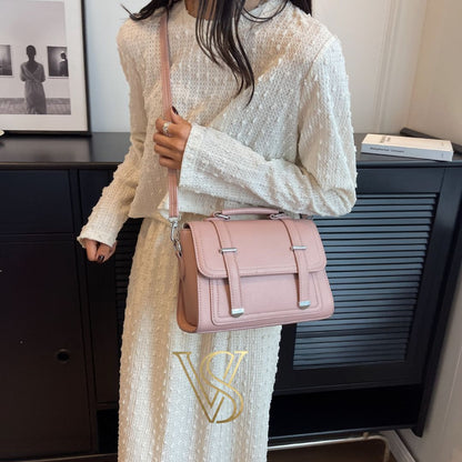 Soft pink crossbody bag with a structured satchel design and silver buckle details.