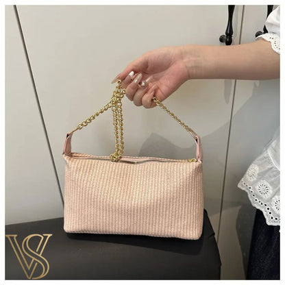 Close-up of a light pink woven straw handbag with a gold chain handle and top zipper.